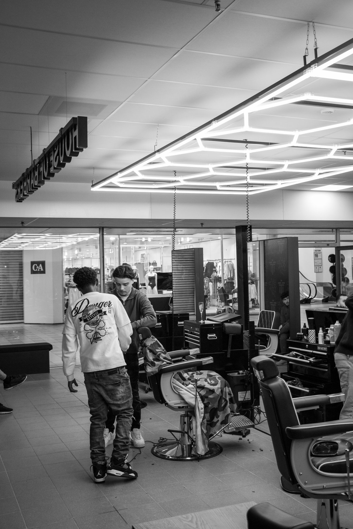 Zwart-witfoto van een barbershop met lege barberstoelen, spiegels en een lamp aan het plafond.