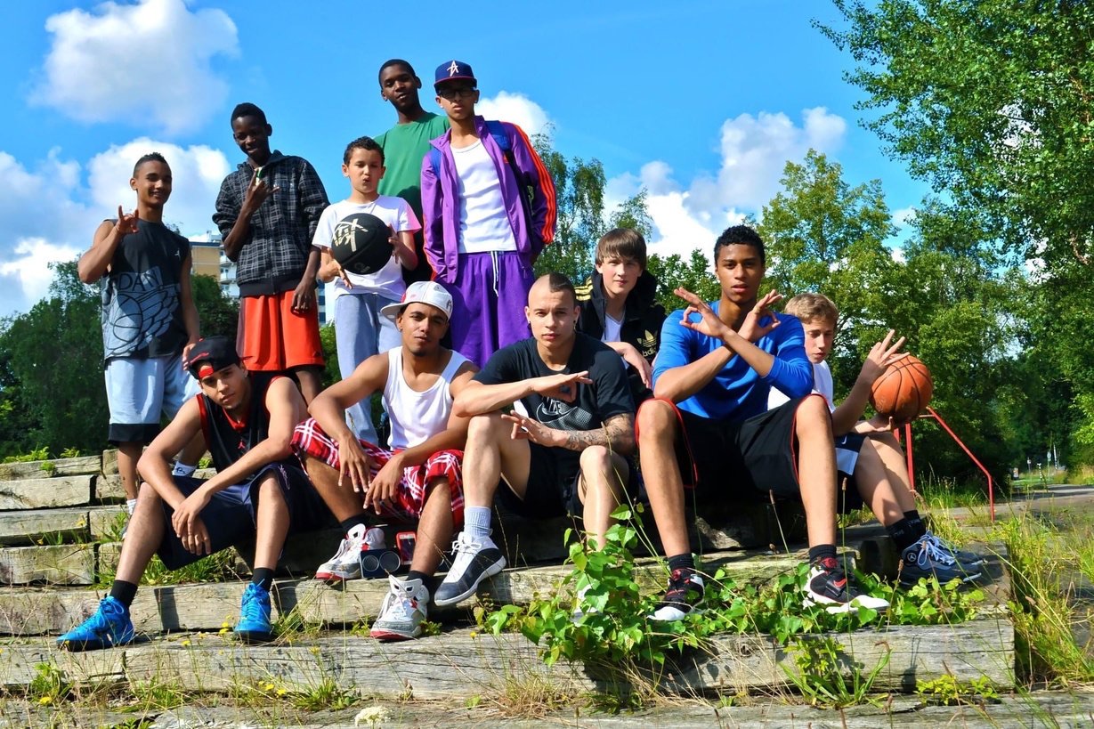 Een groep jonge basketballers zit samen op stenen treden buiten, met ballen in de hand.